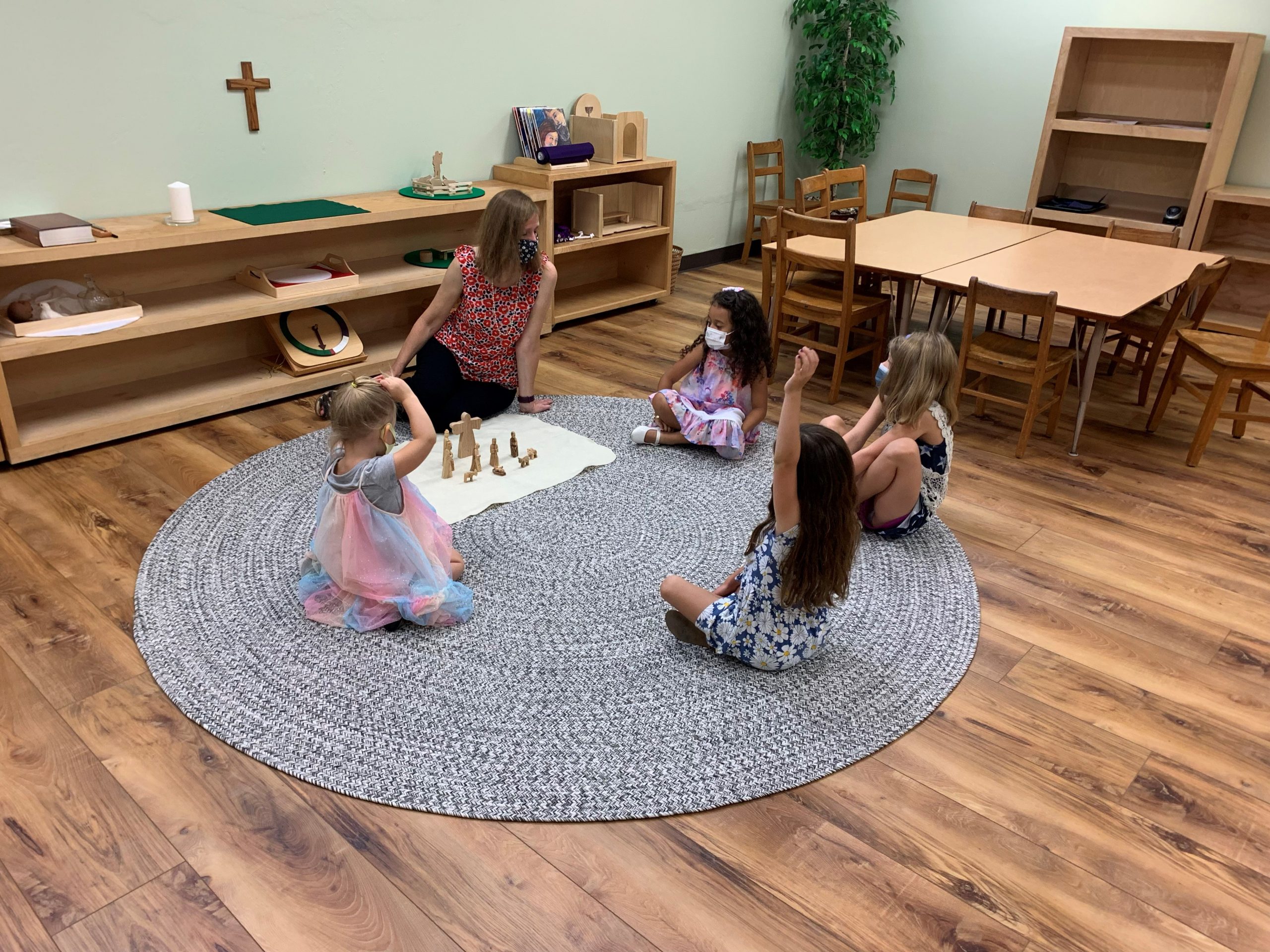 four children and an adult sitting in a circle on a rug with godly play props