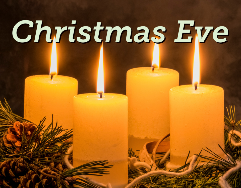 four lit white pillar candles in a pine wreath with the text "Christmas Eve"